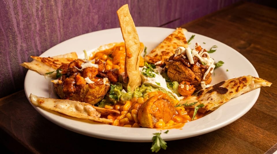 A vibrant platter of Mexican food with quesadillas, guacamole, corn, and meat dishes.