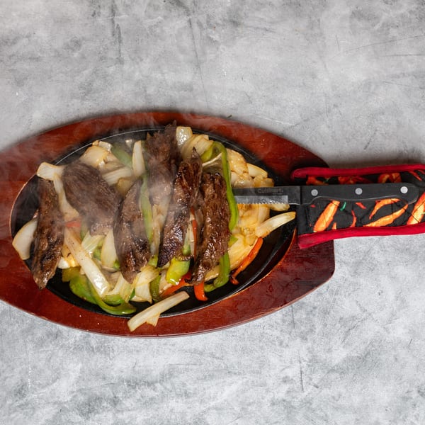 Steaming steak fajitas with colorful peppers and onions on a hot plate with a knife.