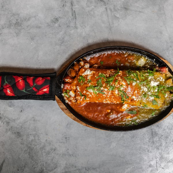 Burrito covered in vibrant red and green sauces, crumbled cheese, and fresh cilantro in a hot skillet.