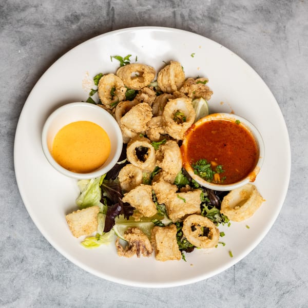 Fried calamari rings and pieces on lettuce with orange and red dipping sauces, and a lime wedge.