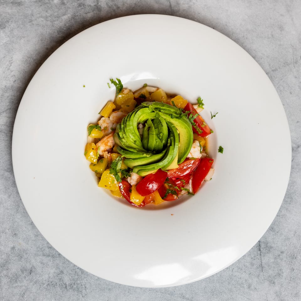 Fresh shrimp, avocado, mango, and tomato salad with herbs in a white bowl.