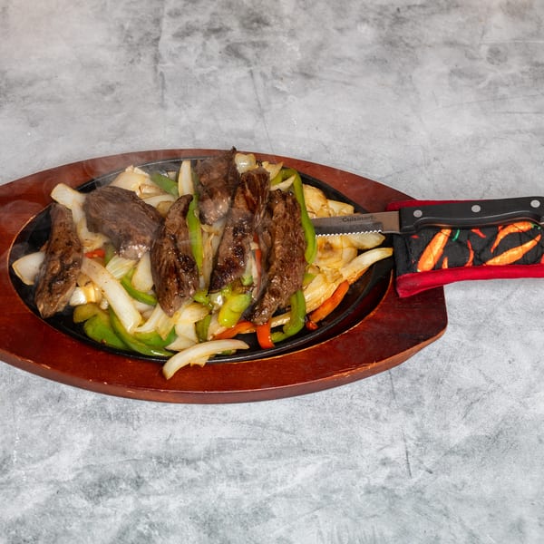 Sizzling steak fajitas with onions and colorful peppers on a hot platter, served with a chili-handled knife.