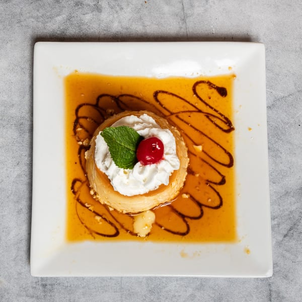 Overhead view of a flan dessert with whipped cream, cherry, and mint, drizzled with caramel and chocolate.