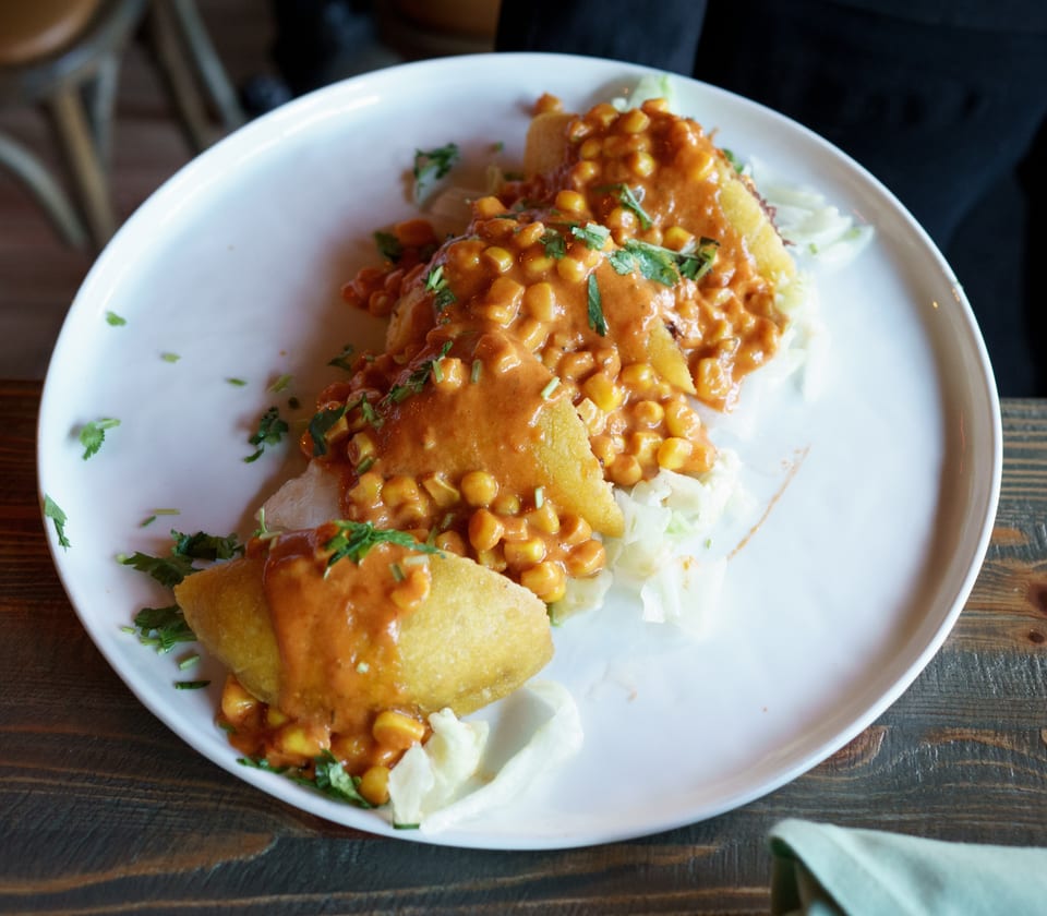 Three golden empanadas topped with creamy corn salsa and fresh cilantro on a white plate.