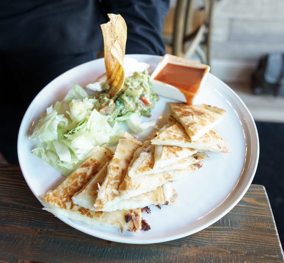 A plate of cheese quesadillas with guacamole, sour cream, lettuce, and salsa.