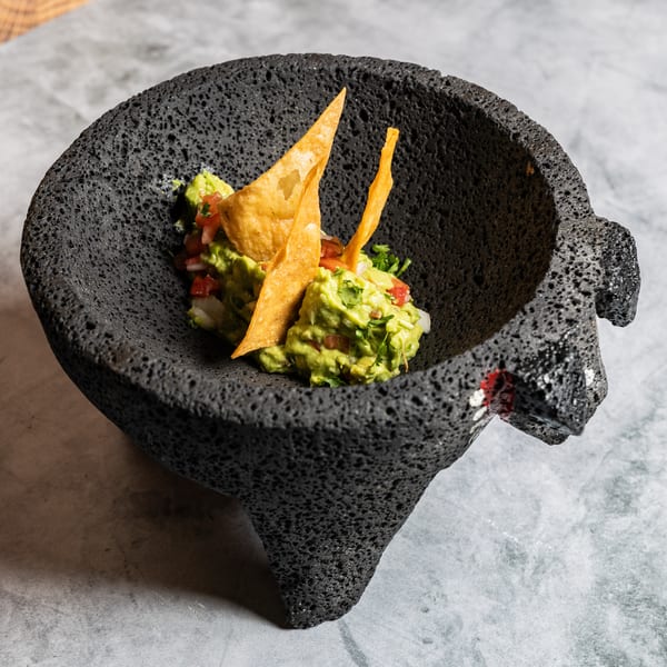 Fresh guacamole with pico de gallo and tortilla chips served in a rustic molcajete.