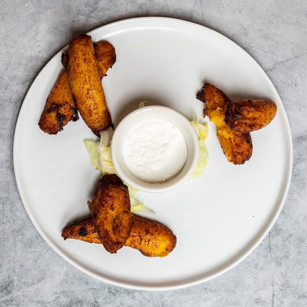 Golden fried plantains with a white dipping sauce and lettuce garnish on a white plate.