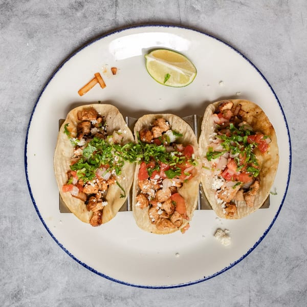 Three chicken tacos with fresh salsa, cilantro, and cheese, served with a lime.