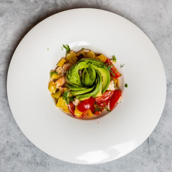 Vibrant shrimp, mango, and tomato salad with a beautiful avocado rose on a white plate.