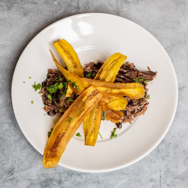 Rice and beans with meat, topped with fried plantains and fresh herbs on a white plate.