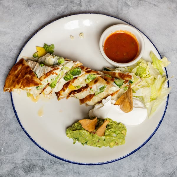 Broccoli and cheese quesadilla slices with salsa, sour cream, guacamole, and lettuce on a white plate.