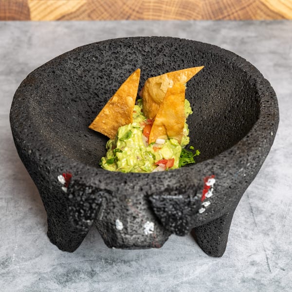 Fresh guacamole with tortilla chips in a textured black molcajete.