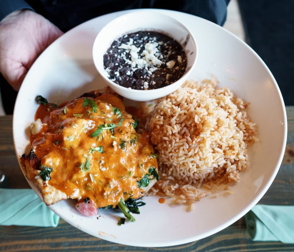 A plate of Mexican food with chicken in red sauce, rice, and a side of black beans.