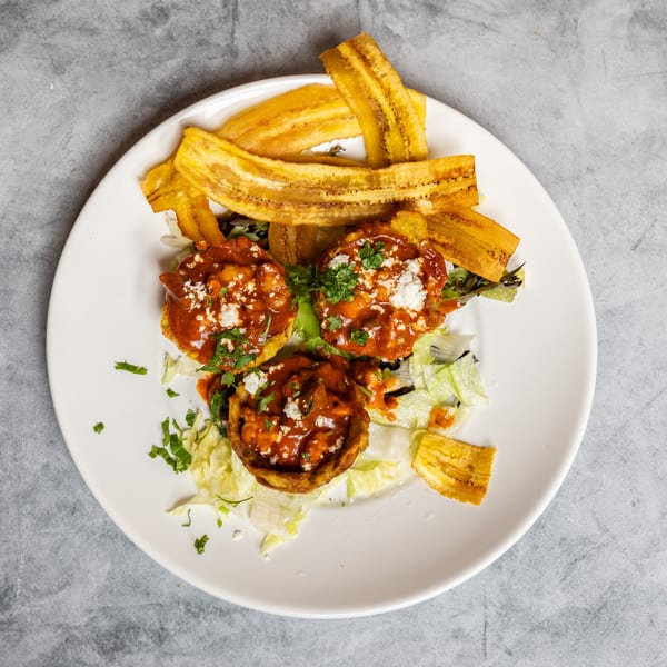 Three fried plantain cups filled with red sauce, cheese, and cilantro, served with plantain chips and lettuce.