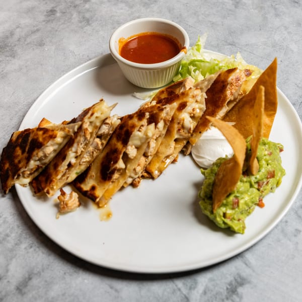 A plate of golden-brown chicken quesadillas, guacamole, sour cream, salsa, and tortilla chips.